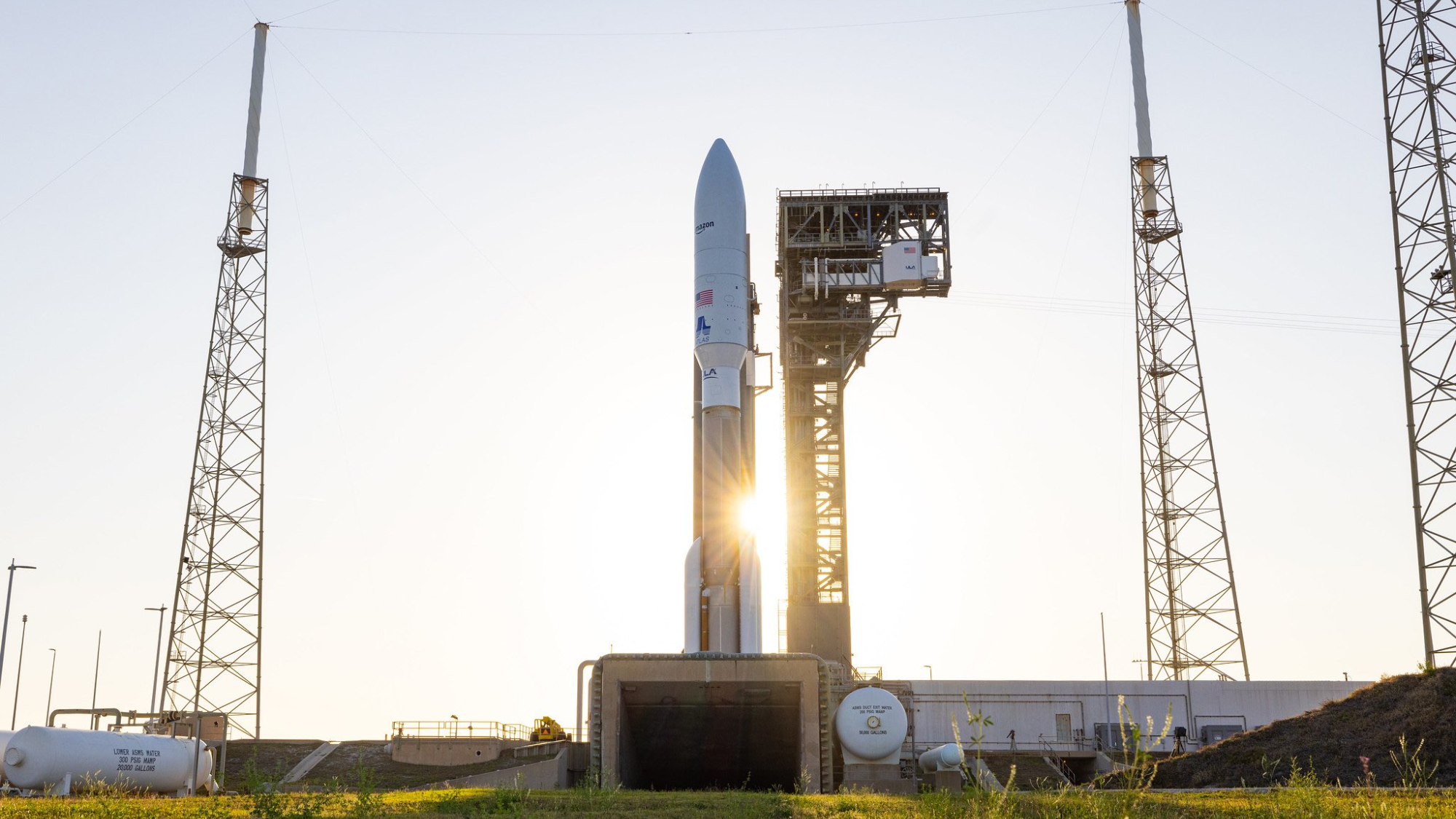 The sun shines behind a white and brown Atlas V rocket carrying Amazon's Kuiper 1 satellites for an April 29, 2025 launch.