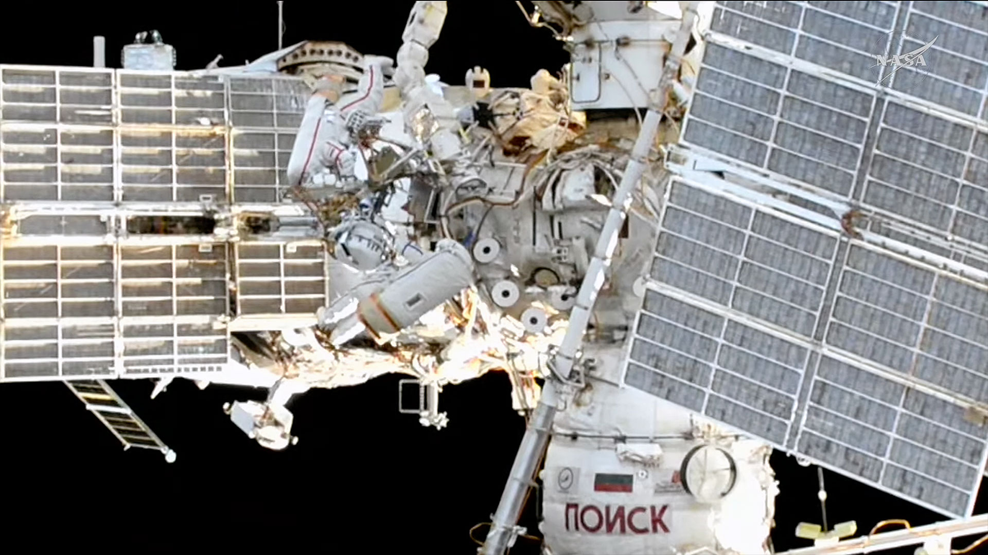 an exterior view of a space station includes two spacesuited cosmonauts at work during a spacewalk