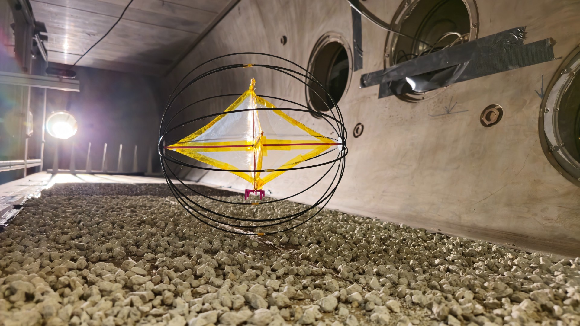 A round cage-like ball encloses a white diamond shape with a yellow outline that rolls over rocks in a dimly lit room.
