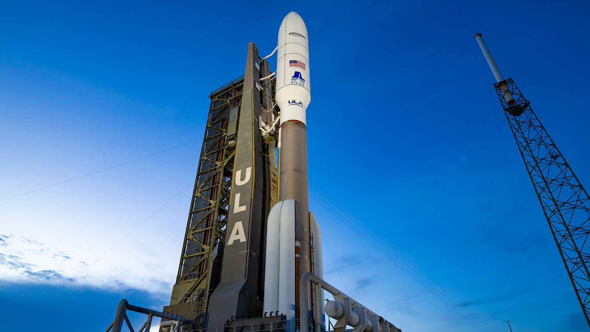 a bronze and white rocket stands poised on its launch pad set against a deep blue sky.