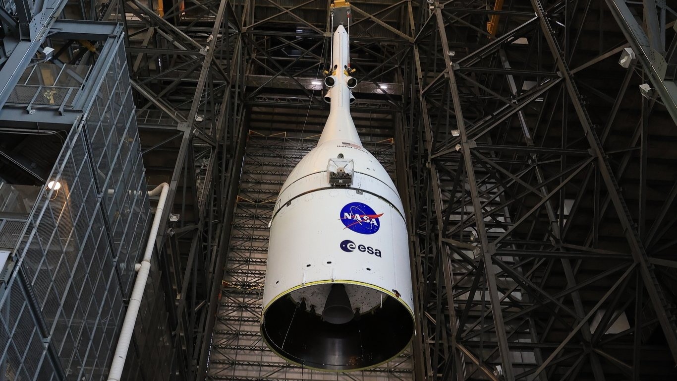 A white cone with NASA and ESA logos is lowered inside a large warehouse bay.