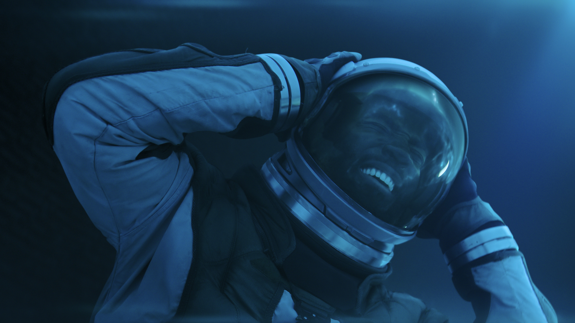 a man grimacing in pain inside a spacesuit