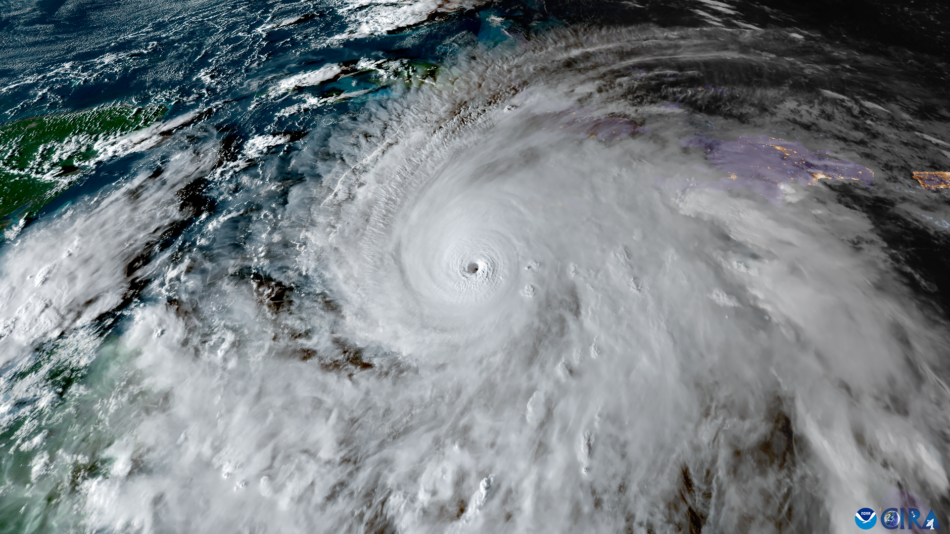 A satellite image showing a large white hurricane headed toward green land in the left side of the image contrasted with the dark blue ocean